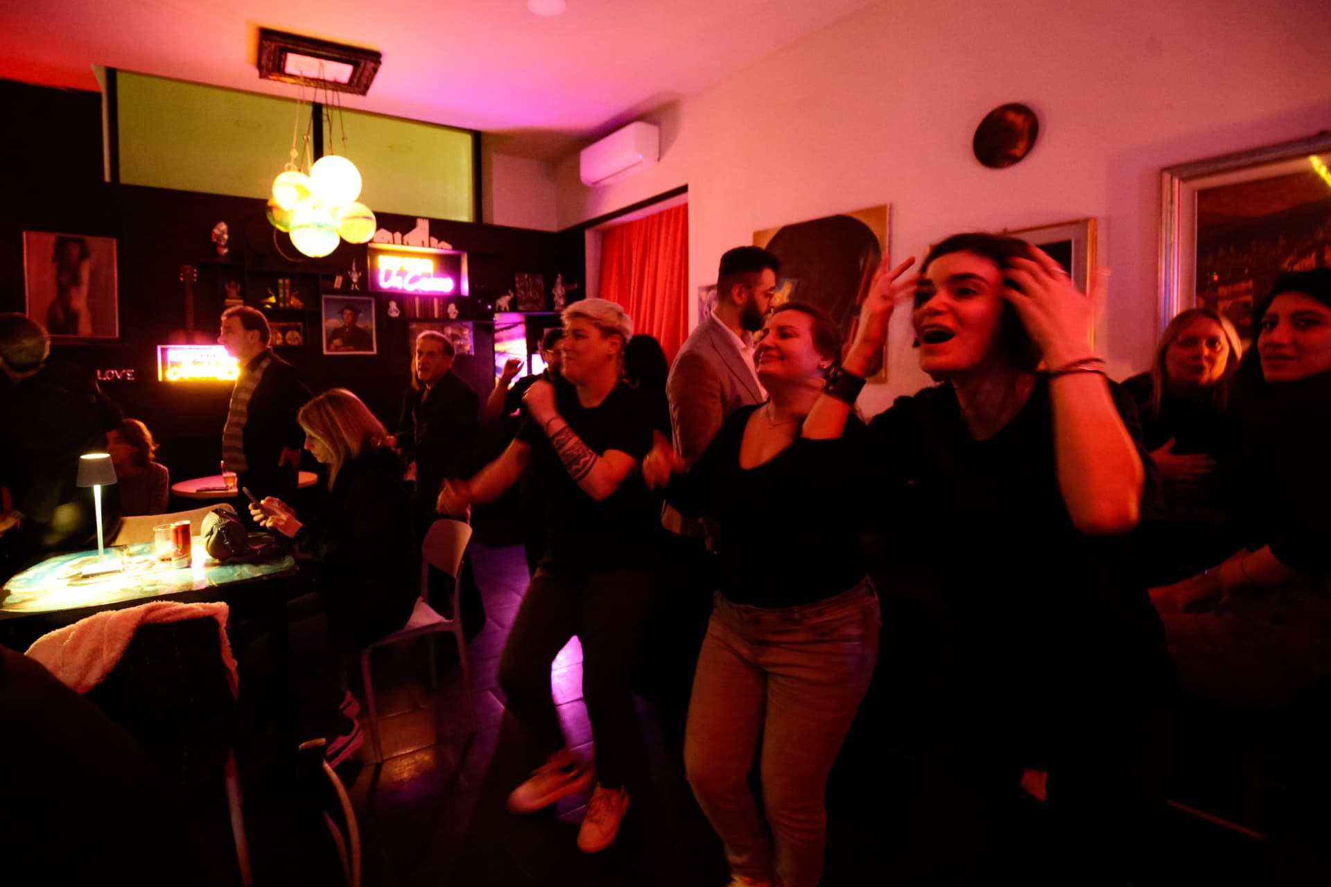 Gruppo di persone che ballano e sorridono durante la notte del Backstage Binasco, con insegna al neon sullo sfondo