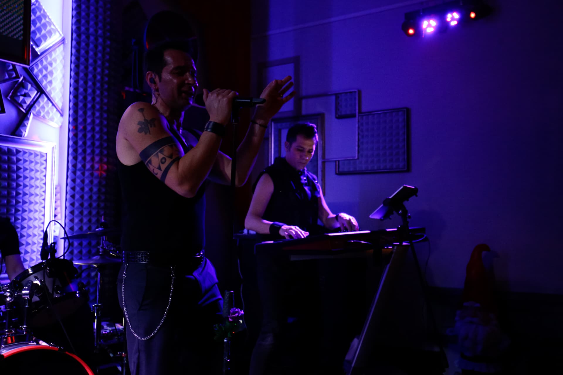 Cantante al microfono e tastierista del Backstage Binasco sotto luce viola e blu durante un live